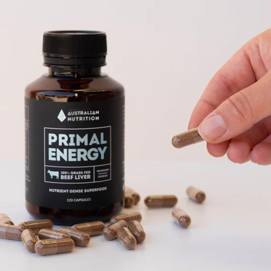 Bottle of Primal Energy beef liver capsules with a hand holding a capsule on a white background